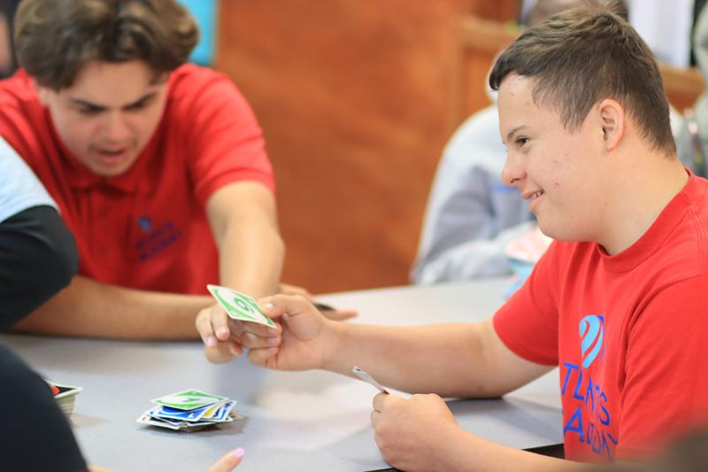 Two students in red Atlantis Academy shirts playing a game of skipbo