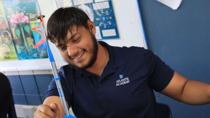 Atlantis Academy adult student smiling at what appears to be a desktop rocket in science class